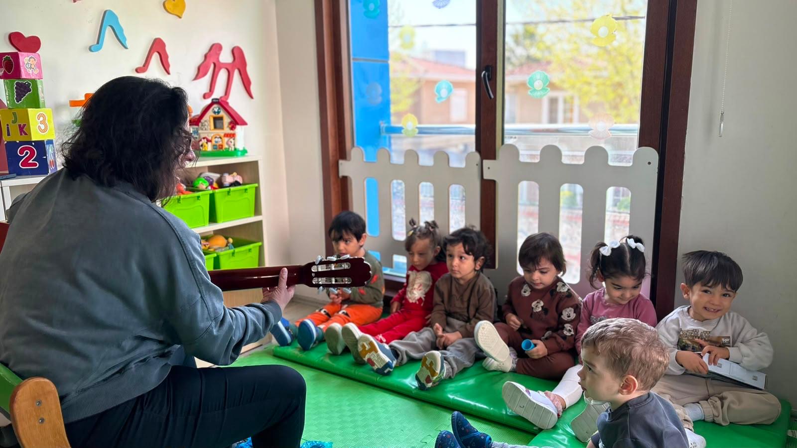 Öğretmen gitar çalarken minik çocuklar dinliyor